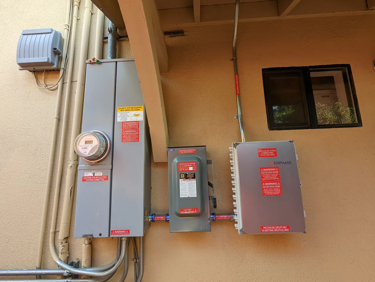 A meter, an alternating current disconnect and a combiner enclosure mounted in a row along a stucco wall, Woodland Hills