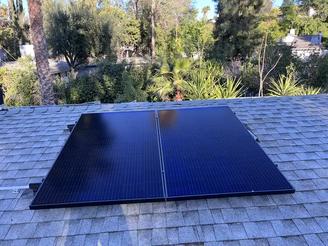 Black solar modules set on a gray composition shingle roof with trees behind, Woodland Hills