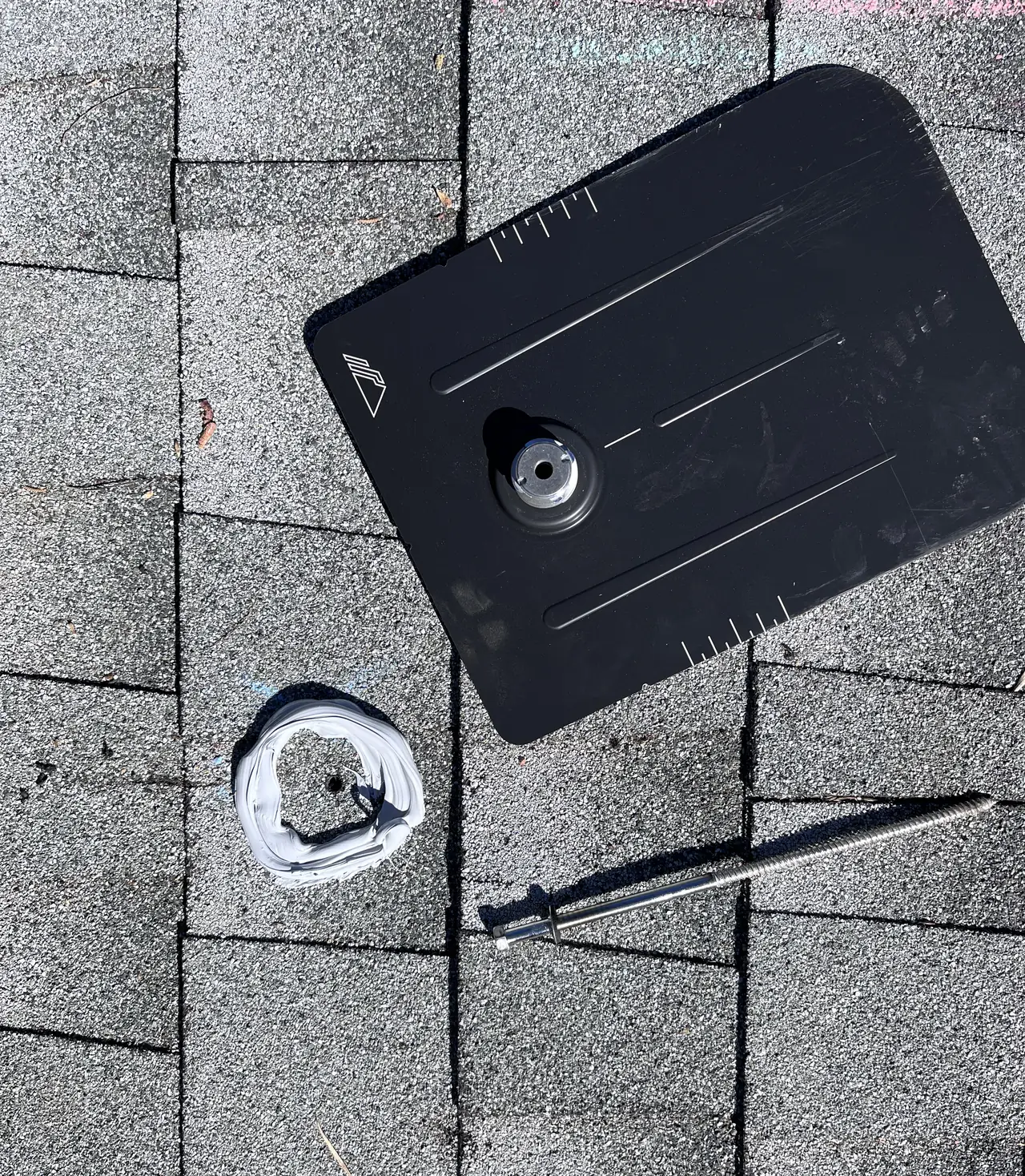 A black flashing plate seated in the shingle course with the mounting hole sealed at its center, Woodland Hills